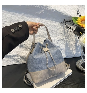 Detail of blue denim bucket bag with grey leather patchwork and drawstring chain closure