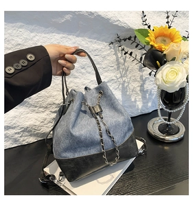 Detail of blue denim bucket bag with black leather base and silver chain drawstring