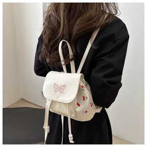 Dettaglio di un mini zaino beige con ricamo a farfalla e stampa di ciliegie su una modella