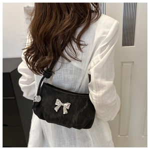 Close-up of black pleated shoulder bag with silver bow accent and beaded strap details