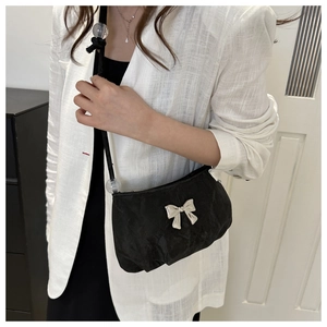 Detail of minimalist black pleated shoulder bag with a metallic silver bow decoration