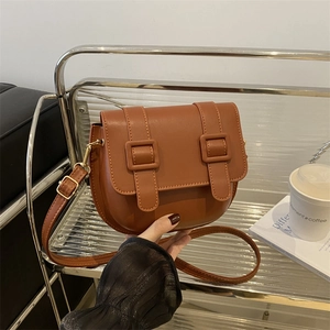 Classic brown crossbody saddle bag with dual buckle straps on a minimalist metal stand