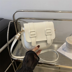 Elegant white saddle crossbody bag with golden hardware on a minimalist silver shelf