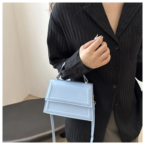 Detail of light blue mini square handbag with top handle held by model in black shirt