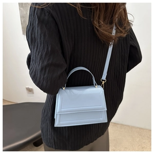 Detail view of a light blue structured crossbody bag with geometric stitching and gold hardware
