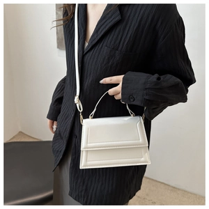 Detailed view of a white leather crossbody bag with geometric stitching on a black shirt