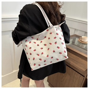 Detail of white tote bag with red strawberry print shown on model's shoulder