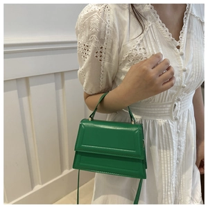 Detailed shot of a green leather crossbody bag worn by a model in a white dress