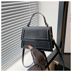 Close-up of matte black small square bag with geometric stitching and adjustable strap