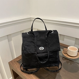 Minimalist black backpack with crinkle texture and oval metal buckle on a coffee table