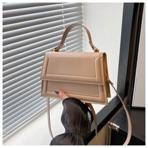 Detailed close-up of beige trapezoid handbag with textured lines and gold-tone metal hardware