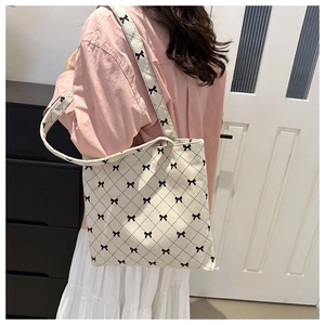 Corduroy tote bag with black bow and diamond pattern worn by a model in a room