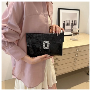 Detail of black crocodile-embossed clutch with shimmering rhinestone square buckle