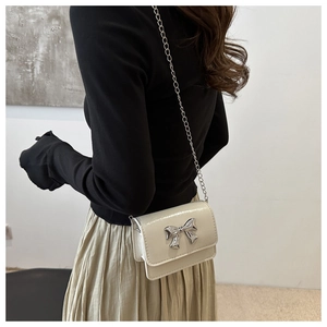 Détail du sac crème brillant avec nœud argenté et bandoulière chaîne sur un mannequin