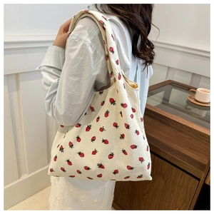 Detail of strawberry print on beige corduroy tote bag worn over the shoulder