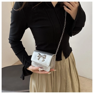 Close-up of silver metallic mini crossbody bag with metal bow detail and chain strap
