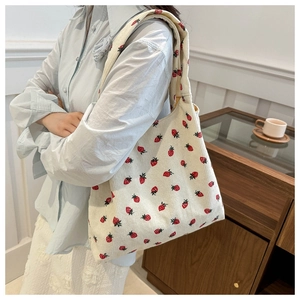 Detail of corduroy tote bag featuring strawberry patterns worn by a model in soft lighting