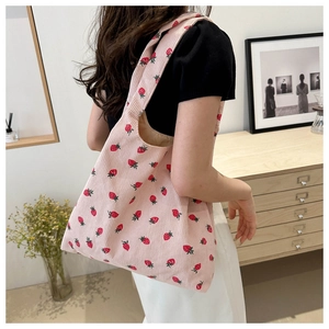Pink corduroy tote bag with red strawberry patterns shown on person in a home setting