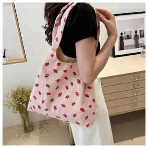 Detail view of pink corduroy tote bag with strawberry print on a model's shoulder