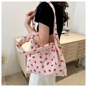 Detail of pink corduroy tote bag with strawberry prints worn over the shoulder