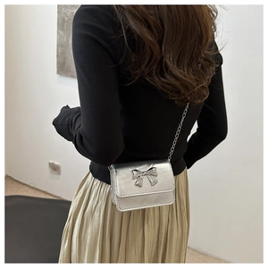 Silver metallic crossbody bag with 3D metal bow detail shown on a female model