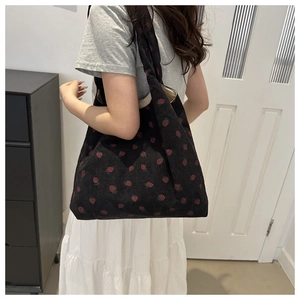 Detail of black corduroy tote bag with red strawberry embroidery on model shoulder