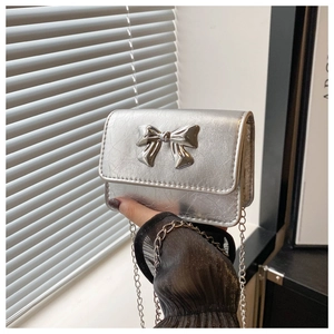 Detail of silver metallic mini bag featuring a 3D bow buckle and textured chain strap