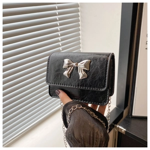 Detail of a mini black oil wax leather chain bag featuring a silver metal bow buckle