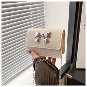 Detail of a creamy white crossbody bag featuring a silver metal bow buckle and chain strap