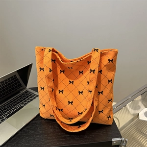 Orange corduroy tote bag with black bow embroidery and diamond quilting on a desk
