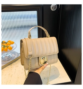 Détail du sac en cuir à rayures avec fermoir rond doré et bandoulière en chaîne métal