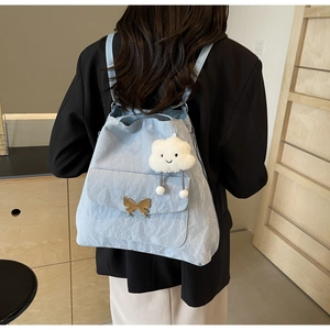 Close-up of light blue textured backpack with golden butterfly buckle and cloud pendant