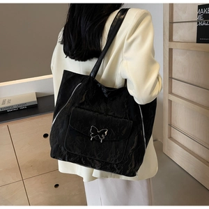 Detail of black pleated tote bag with silver butterfly buckle on a textured shoulder strap