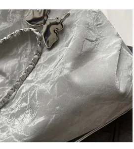 Detail of silver metallic crinkled fabric with a butterfly charm and chain strap
