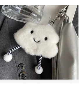 Dettaglio di un ciondolo a nuvola in peluche bianco con sorriso su una borsa a mano