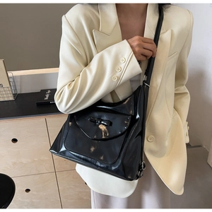 Dettaglio della borsa tote in pelle verniciata nera con elegante fiocco e tracolla comoda