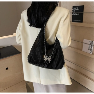 Detail of black pleated tote bag with silver butterfly charm and chain strap detail