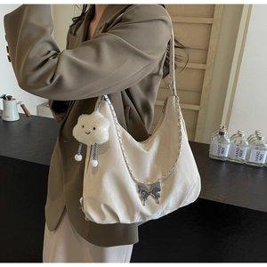 Detail of soft cream crescent tote bag featuring silver chain and butterfly pendant