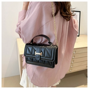Detail of black quilted crossbody bag with gold chain strap and H-shaped buckle closure