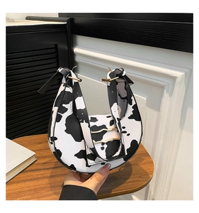 Detalle de bolso medialuna con estampado de vaca, piel PU lisa y hebilla de metal dorado