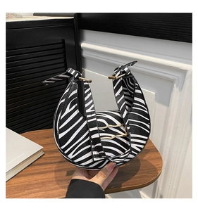 Detalle de bolso medialuna de cebra con herrajes dorados y asa superior ajustable