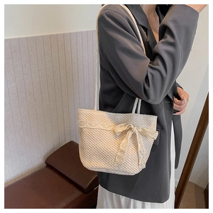 Detail of cream woven tote bag featuring delicate lace edges and a large lace bow accent