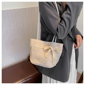 Detail of beige straw shoulder bag featuring intricate lace trim and a large bow accent