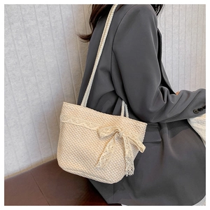 Detail of beige woven straw tote bag featuring delicate lace trim and ribbon bow accent
