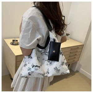 Detail of white butterfly print tote bag with mini pouch worn by a model in a cozy room