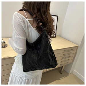 Detail of black pleated tote bag with wooden bead strap accents for a vintage look