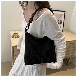Detail of black pleated shoulder bag with unique wooden bead strap and woven texture