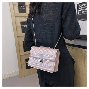 Close-up of quilted pale pink crossbody bag with silver chain strap worn by a person