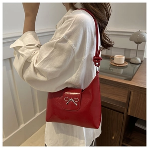 Détail du sac à bandoulière en cuir verni rouge avec boucle nœud argentée et sangle nouée