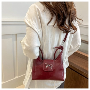 Detail of dark red shoulder bag with silver bow accent and knot shoulder strap design